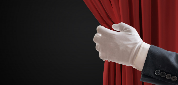 Actor is pulling red curtains in theatre with hand. white glove