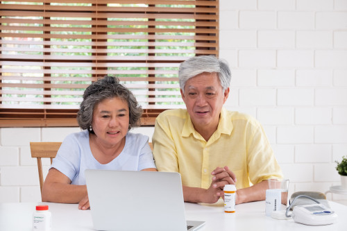 Asian couple seniors use laptop video conference with doctor about illness and prescription pill in living room at home
