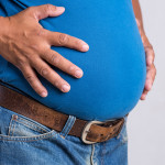 Overweight or fat adult man in very tight jeans on a gray background. Healthcare, medicine