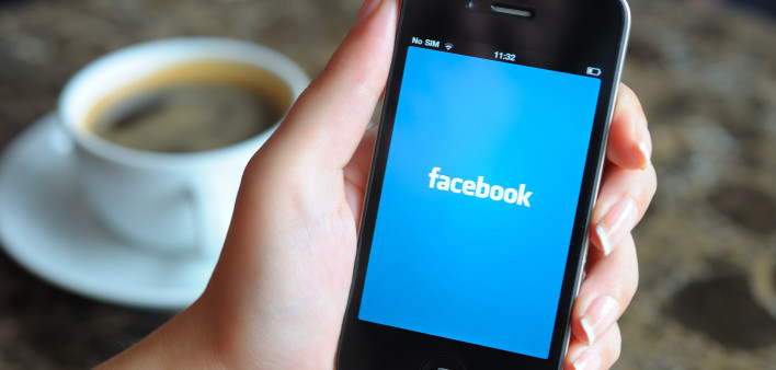 Woman hand holding an Apple iPhone 4 in a coffee shop. iPhone 4 displaying start up screen of Facebook application.