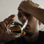 Drunk young adult male holding glass of alcohol, studio shot.