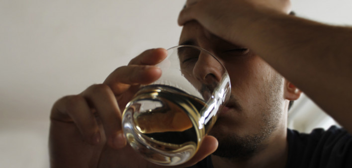 Drunk young adult male holding glass of alcohol, studio shot.