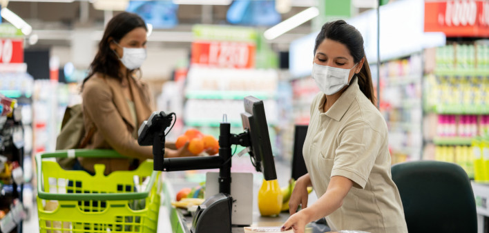 Latin American cashier scanning products at a grocery store wearing a facemask - quarantine lifestyle