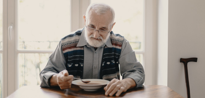 Sad lonely senior man eating soup in empty apartment