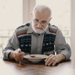 Sad lonely senior man eating soup in empty apartment