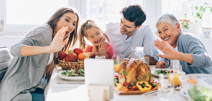 Happy multi-generation family sitting at the dining table on Thanksgiving and communicating through a digital tablet