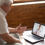 Focused older 80s male patient consulting with doctor via computer video call.