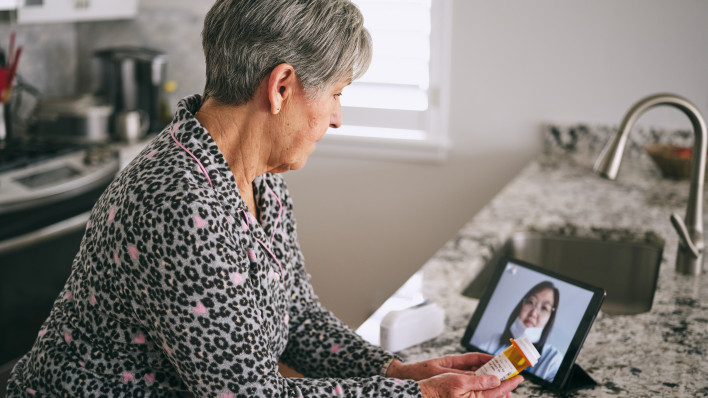 A senior aged woman in her home, talking to a doctor online in a virtual appointment.