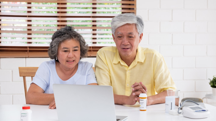 Asian couple seniors use laptop video conference with doctor about illness and prescription pill in living room at home