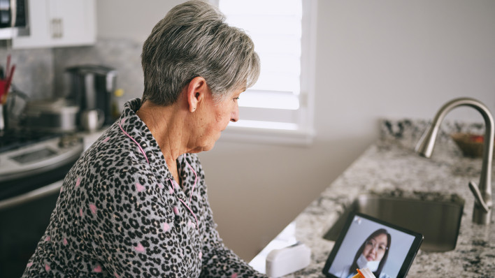 A senior aged woman in her home, talking to a doctor online in a virtual appointment.