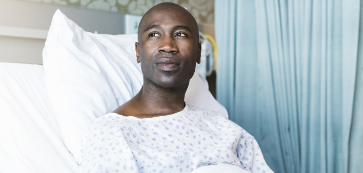 Thoughtful patient lying on bed. Mid adult man is wearing hospital gown.