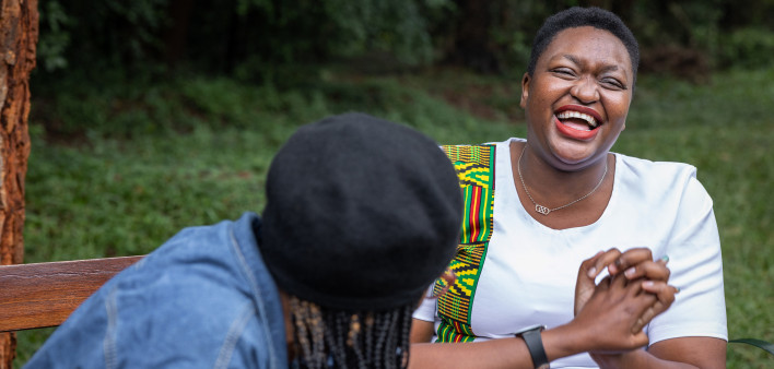 Two friends enjoying a laughing while having a conversation on a park bench in Nairobi, Kenya, the woman on the right is living with HIV