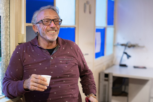 A smiling senior man living with HIV drinking coffee in an office