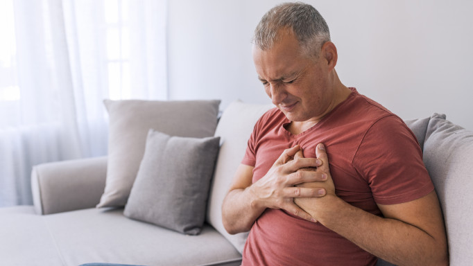 Severe heartache, man suffering from chest pain, having heart attack or painful cramps, pressing on chest with painful expression. Photo of Mature man suffering from chest pain at home during the day.