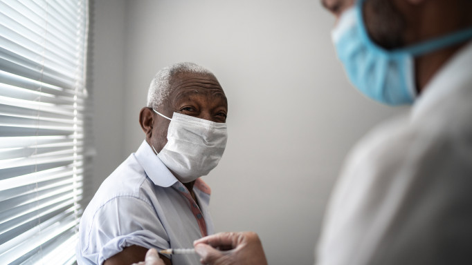 Nurse applying vaccine on patient's arm using face mask