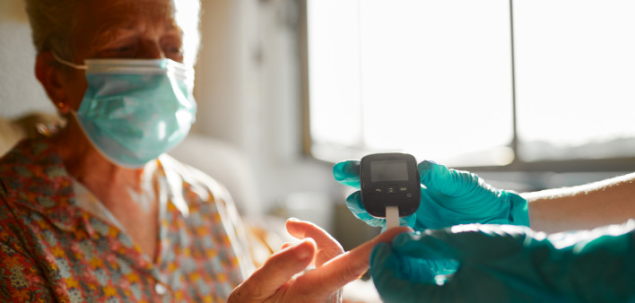 A nurse helping a senior woman perform a diabetes test