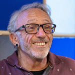 A smiling senior man living with HIV drinking coffee in an office