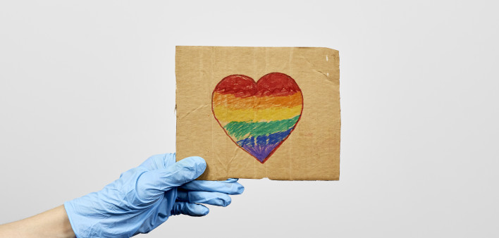 LGBTQ friendly healthcare system worker holding handmade placard with heart-shaped rainbow flag.