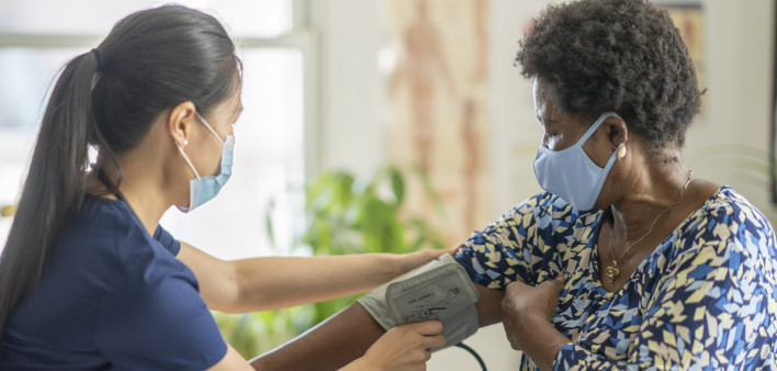 Asian nurse using a blood pressure gauge to check an African American, elderly woman's health.