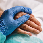 doctor hand with blue glove giving support and love to a patient at hospital. Coronavirus
