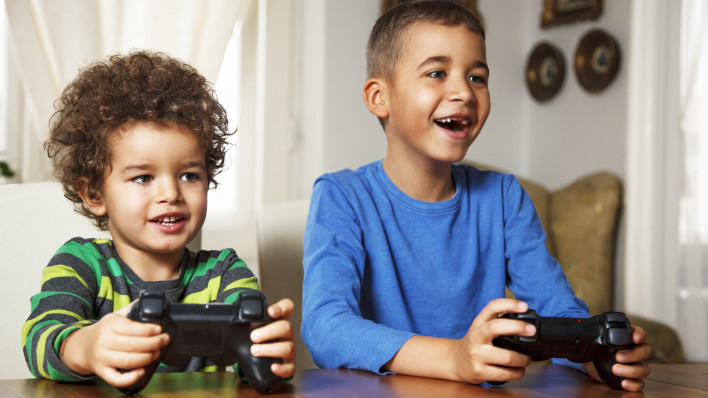 Afro American boys playing video games at home. They having fun, playing computer games, holding joysticks in hands and making funny faces.