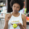 Beautiful black woman eating a healthy bowl and a green apple at the gym