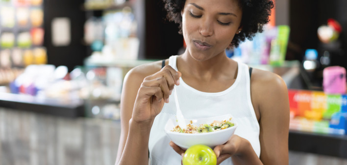 Beautiful black woman eating a healthy bowl and a green apple at the gym