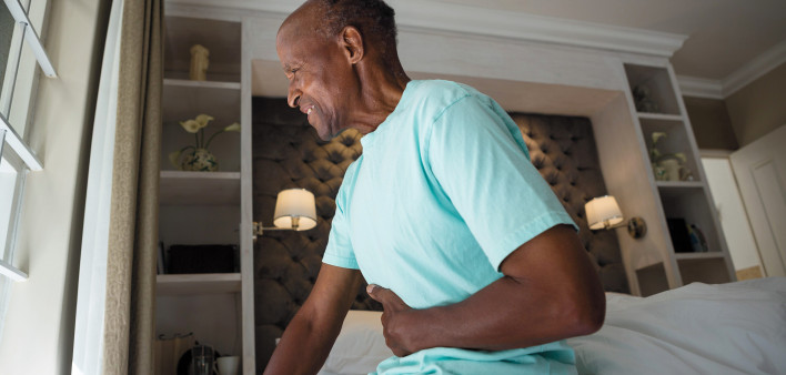 man in bed with belly pain holding stomach