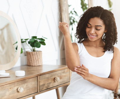 Dry Elbows Treatment. Smiling Black Woman Applying Moisturising Cream