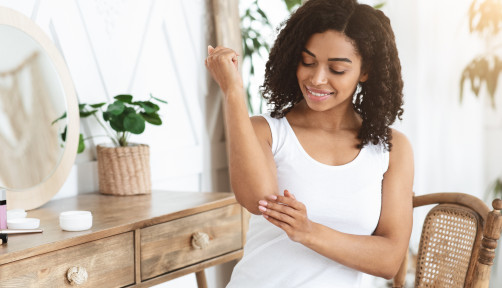 Dry Elbows Treatment. Smiling Black Woman Applying Moisturising Cream