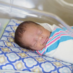 Sleeping baby boy resting in a hospital crib in a hospital delivery room.