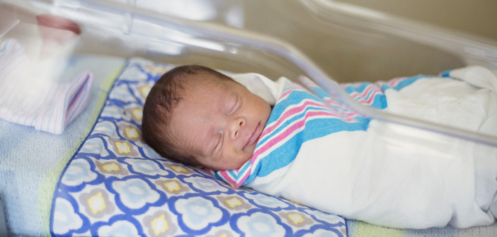 Sleeping baby boy resting in a hospital crib in a hospital delivery room.