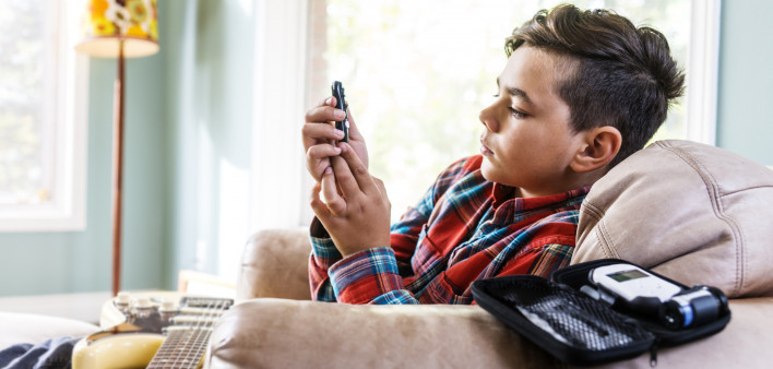 Diabetic child testing his blood sugar in his living room. A guitar is on his lap.