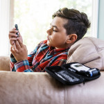 Diabetic child testing his blood sugar in his living room. A guitar is on his lap.
