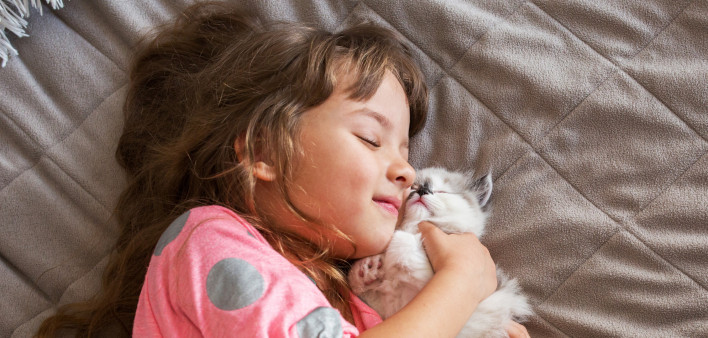 Happy girl is hugging her kitten indoors.