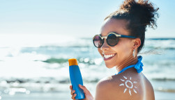 Portrait of a beautiful young woman with a sun drawn on her shoulder with sunscreen at the beach
