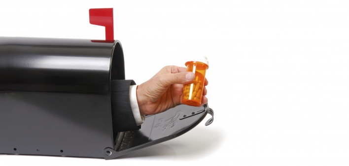 a hand holding a prescription coming out of a mailbox