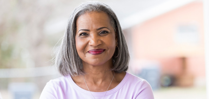 Beautiful African American senior woman stands confidently on her front porch. She is smiling at the camera.