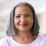 Beautiful African American senior woman stands confidently on her front porch. She is smiling at the camera.