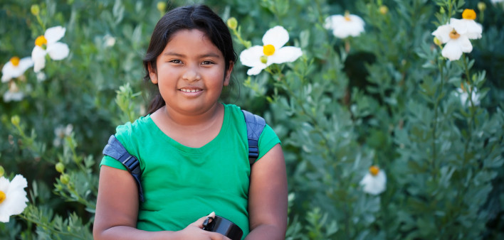 A 9 year old child or student wearing a backpack and holding a thermos