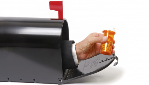a hand holding a prescription coming out of a mailbox