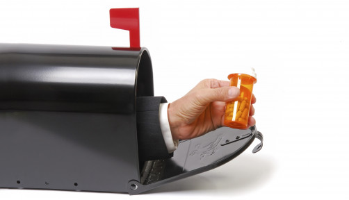 a hand holding a prescription coming out of a mailbox