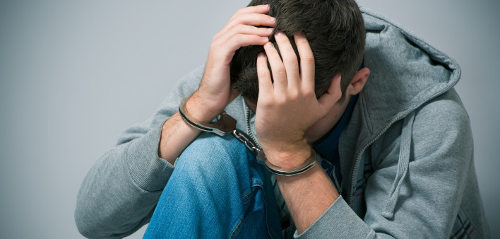 A handcuffed teenager holding his head in shame stock