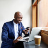 Portrait of happy african businessman using phone while working on laptop in a restaurant