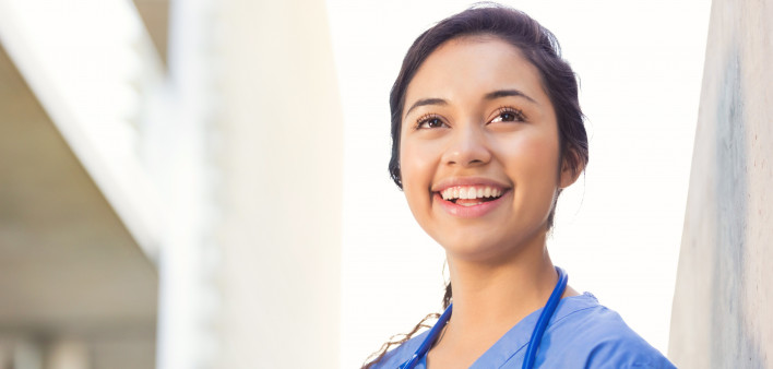 Young adult Hispanic woman is smiling while standing outside on college campus.