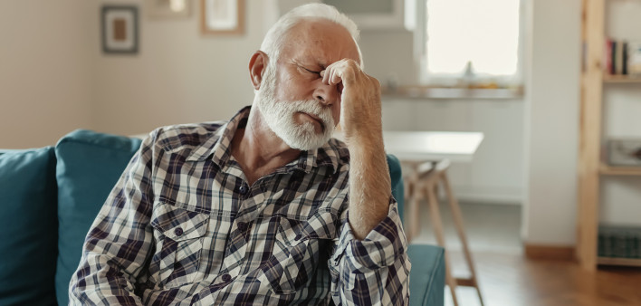 A Distraught Senior Man Suffering From a Migraine While Sitting on the sofa in the Living Room