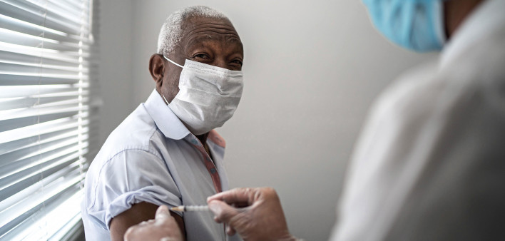Nurse applying vaccine on patient's arm using face mask