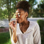happy african american woman smoking marijuana joint in back yard
