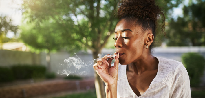 happy african american woman smoking marijuana joint in back yard