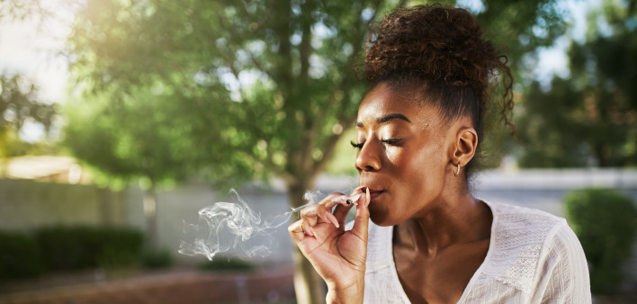 happy african american woman smoking marijuana joint in back yard